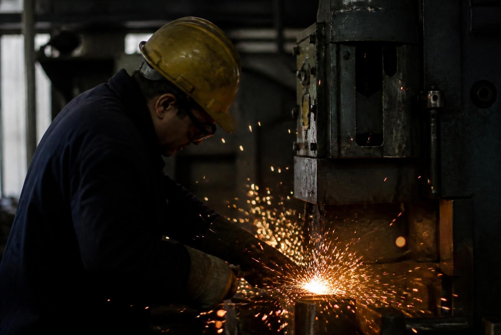 Arbeiter an einer Maschine in einer Industriehalle, Funkenflug im dunklen Licht